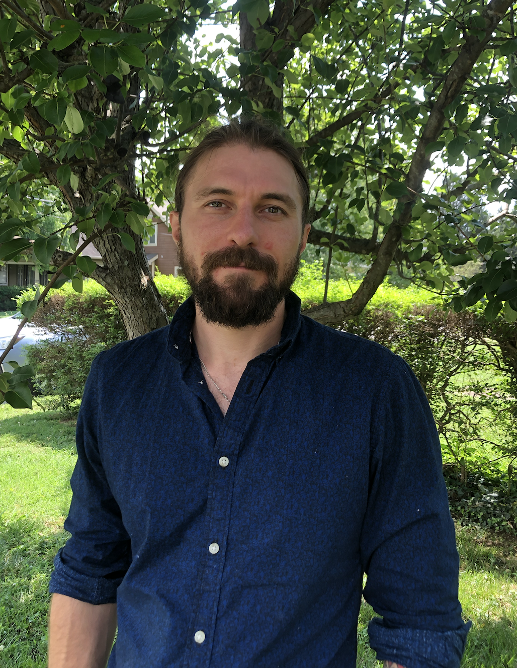 A picture of Slava in a blue shirt in front of green bushes